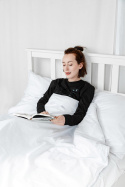 kobieta czytająca książkę na łóżkku przykryta jest kołdrą obciążeniwą w kolorze białym