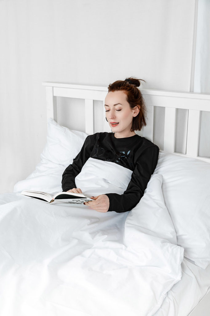 kobieta czytająca książkę na łóżku przykryta jest kołdrą obciążeniową w kolorze białym
